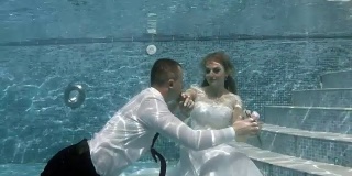 幸福的新郎和新娘穿着白色婚纱坐在池底。新郎飘起来，亲吻新娘的手