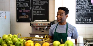 在果汁吧工作的黑人推销员传递一个绿色果汁给一个看起来非常高兴和微笑的不认识的顾客