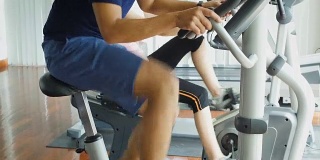 年轻的亚洲健身男子使用自行车在健身房锻炼自行车，有氧训练概念，倾斜相机拍摄
