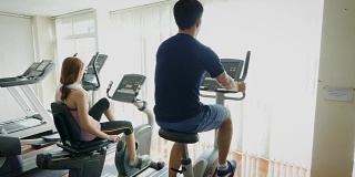 年轻的健身夫妇使用自行车运动自行车在健身房，有氧训练的概念