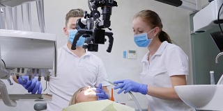 专科医生和助手在牙科室使用光学显微镜对躺着的病人进行口腔手术