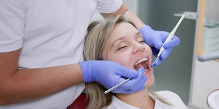 医疗诊所，美丽的女人张着嘴在牙科医生的检查与牙科仪器在手近距离