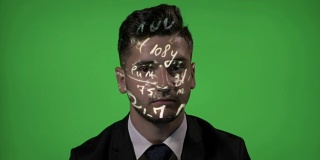 年轻的男大学教授使用增强现实的数学全息公式投影在他的脸在绿色屏幕的背景