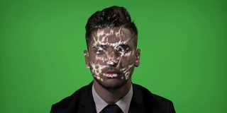 年轻的男大学生使用增强现实有化学全息公式投影在他的脸在绿色屏幕背景
