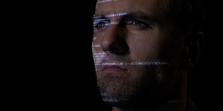 一个程序员软件开发人员在黑暗的房间工作，而计算机代码反映在他的脸上的特写
