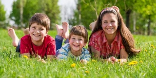 三个微笑的孩子一起躺在绿色的草地上