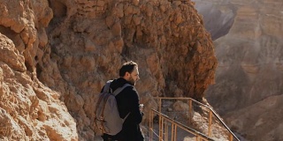 古山路上的白人男性游客。手持智能手机和相机的男子欣赏以色列沙漠遗址。4 k