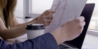 在服务台的女人手里拿着一支笔给男人看一张纸上的图表