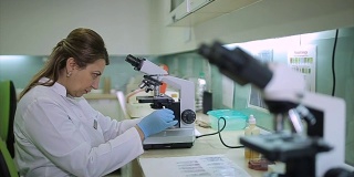 女科学家通过实验室的显微镜看微生物学