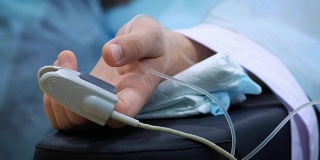 病人的手在床上与血氧计。抢救病人，在手术中测量脉搏和血压。