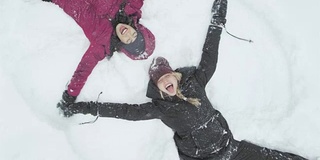 两个年轻漂亮的女人躺在雪地上，堆着雪天使