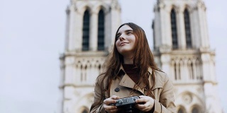 在法国巴黎，著名的大教堂里，美丽的少女在复古胶片相机上拍摄巴黎圣母院的照片