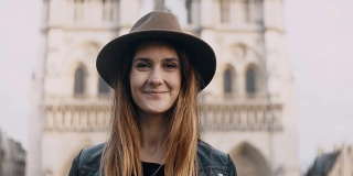 在巴黎圣母院附近的年轻美丽的女人戴着帽子的肖像，法国。女性看着镜头微笑