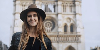 一幅年轻美丽的女人戴着帽子站在巴黎圣母院附近的肖像，法国看着镜头
