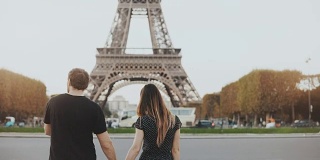 在法国巴黎，一对年轻幸福的情侣在埃菲尔铁塔附近散步。男人和女人在街上拥抱亲吻