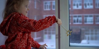 可爱的小女孩坐在窗台上，望着外面的雪景。