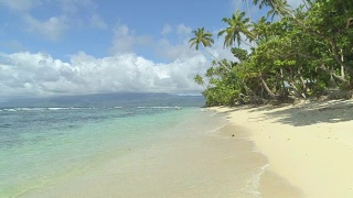 低角度视角:泡沫波浪翻滚向斐济岛的沙海岸线。视频素材模板下载