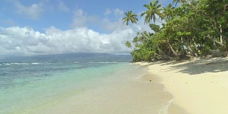 低角度视角:泡沫波浪翻滚向斐济岛的沙海岸线。
