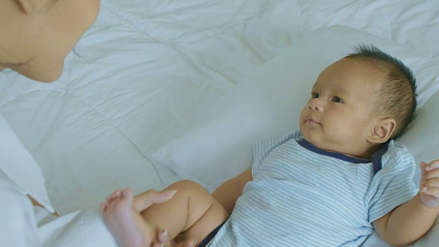 年轻的亚洲母亲与躺在床上的婴儿儿子玩耍。