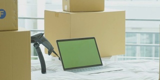 摄影:笔记本电脑与绿色屏幕色度键放在床上与纸板箱环绕，在线经营理念。