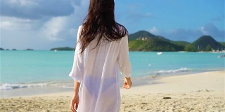 年轻漂亮的女人在热带海岸玩。在海滩上戴帽子的女孩的背影。慢动作