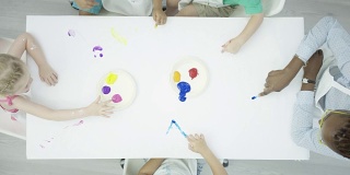 一群孩子在干净的白色桌子上画手指画
