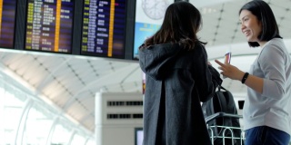 两名女子在机场候机楼碰面，检查电子登机牌上的航班