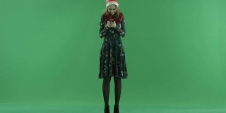 年轻可爱的女人戴着圣诞帽在她的智能手机上发短信，色度键在背景上