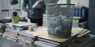 一个女人在办公室工作，她把丢弃的文件弄皱，扔进垃圾桶