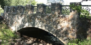 在一个晴朗的夏日，公园里的石桥在一条干涸的小溪上