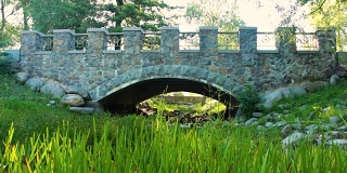 在一个晴朗的夏日，公园里的石桥在一条干涸的小溪上