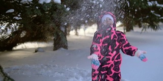 一个快乐的孩子穿着连体衣玩雪花飘落的树，慢镜头。