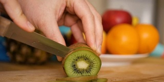 男子用刀在木板上切猕猴桃，背景是水果和蔬菜。特写镜头。