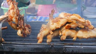 把整只鸡串在木棍上，放在烤架上烤制。泰国的街头食品。男人的手翻着烤鸡视频素材模板下载