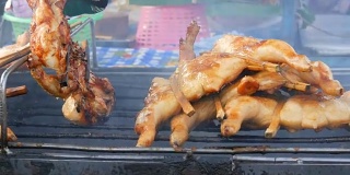 把整只鸡串在木棍上，放在烤架上烤制。泰国的街头食品。男人的手翻着烤鸡