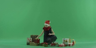 可爱的小女孩在圣诞帽试图选择圣诞礼物，色度键的背景