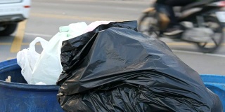 那个女人扔了一个塑料瓶。满垃圾桶的大垃圾袋装满了剩菜和垃圾在街上