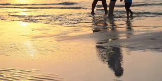 日落时分，在阳光下，一对夫妇带着一个小孩沿着海滩散步，沿着冲浪线。他们的剪影映在水中