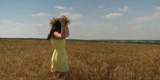 在阳光明媚的日子里，一个头戴麦冠、身穿黄裙的女人在金黄的麦田里旋转