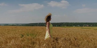 在阳光明媚的日子里，身着黄裙，头戴麦冠的女人走在金色的麦田里。镜头从麦穗上方升起