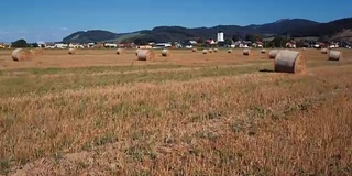 在有圆草堆的田野上空低空飞行。风景如画的小村庄和山峦为背景。