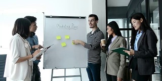 在现代办公室开会期间，年轻的商业人士在白板上用便利贴与他们的同事分享商业战略计划的想法。