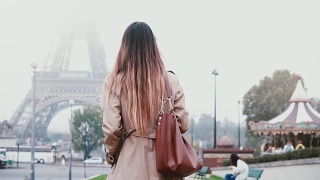 后视图的年轻女子穿着法国风格步行到埃菲尔铁塔在巴黎，法国。女孩看着著名的风景视频素材模板下载