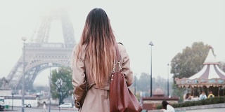 后视图的年轻女子穿着法国风格步行到埃菲尔铁塔在巴黎，法国。女孩看着著名的风景