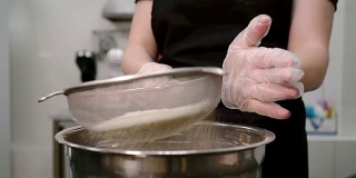 一名年轻女子在厨房用筛子筛面粉