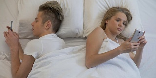 夫妻背靠背躺在床上玩着智能手机，玩着社交网络，视而不见