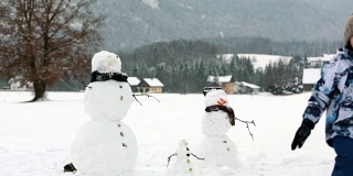 一家人带着孩子，在奥地利小村庄的公园里堆雪人，风景秀丽。