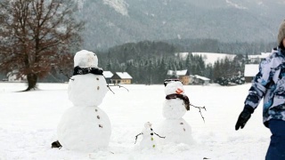 一家人带着孩子，在奥地利小村庄的公园里堆雪人，风景秀丽。视频素材模板下载