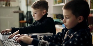 两个小男孩试着打字，学习如何使用笔记本电脑。对儿童的替代性编程教育。