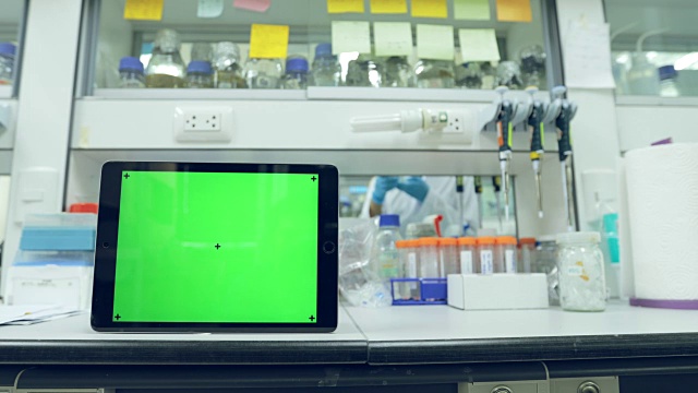平板绿色屏幕背景与科学家在实验室工作